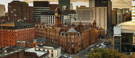 A cityscape with a mix of historic and modern buildings, including a prominent red brick building with a clock tower and a modern glass skyscraper.