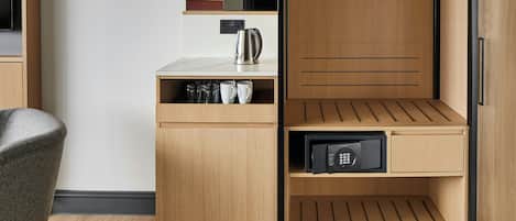 A modern hotel room with a wooden wardrobe, a small kitchenette, and a seating area.