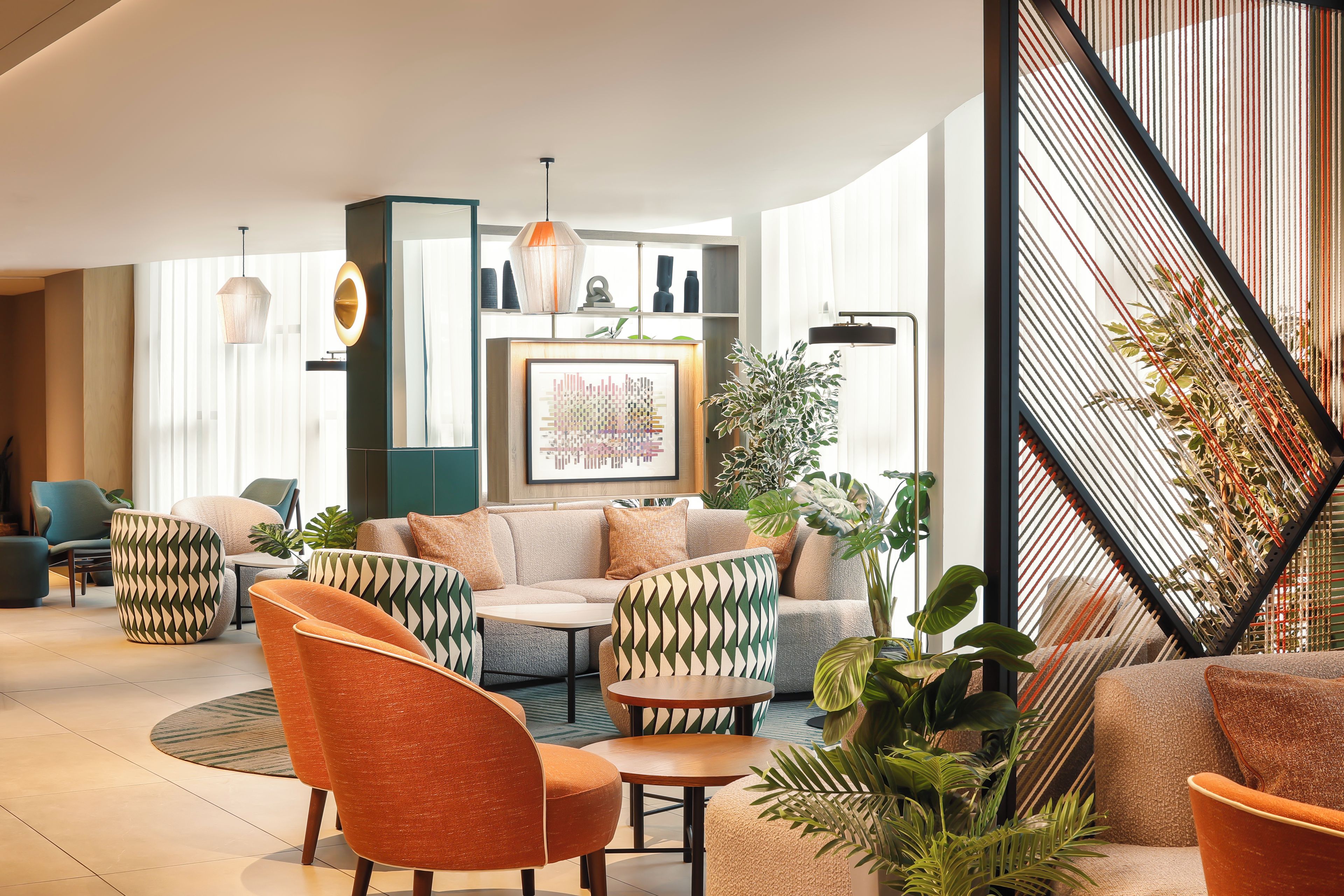 A modern living room with a sofa set, a coffee table, and a patterned armchair. There is a large painting on the wall and a potted plant in the corner.