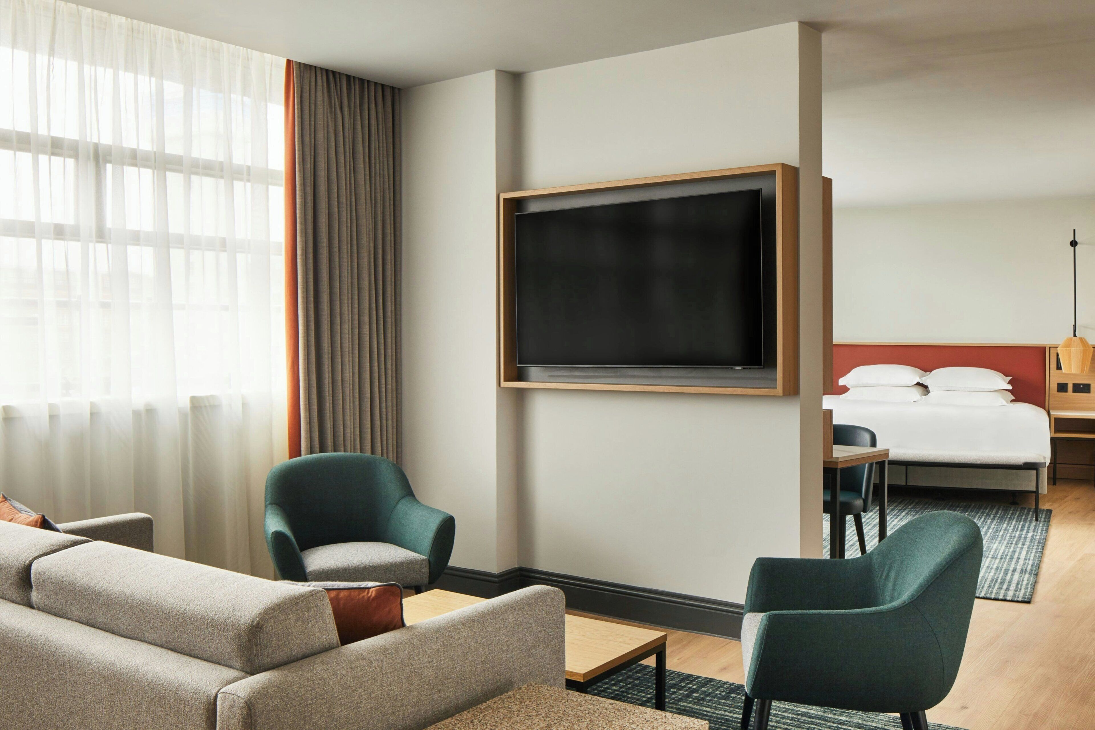 Una habitación de hotel con una cama grande, un televisor montado en la pared, un sofá, dos sillones y una mesita.