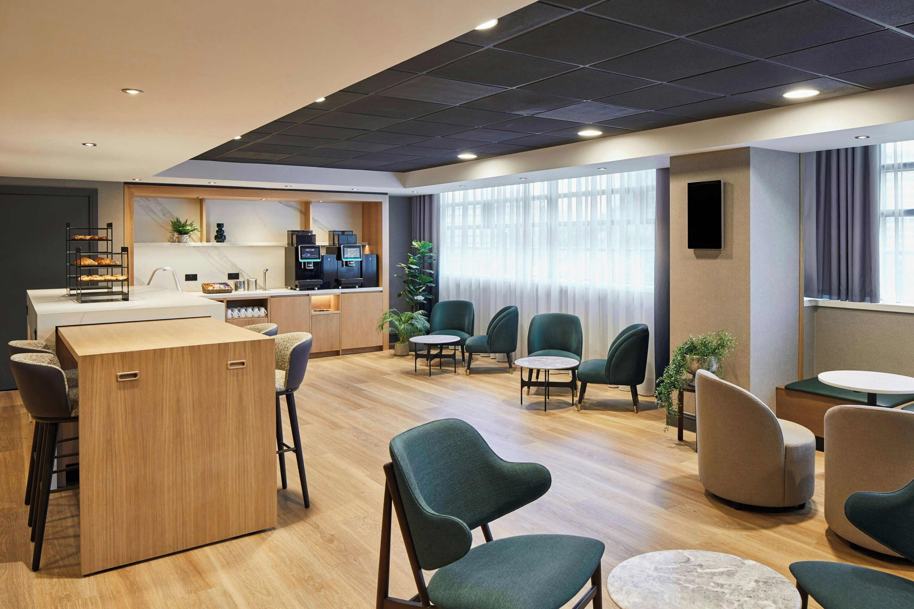 A modern hotel lobby with a wooden reception desk, multiple seating areas, and a large window with curtains.