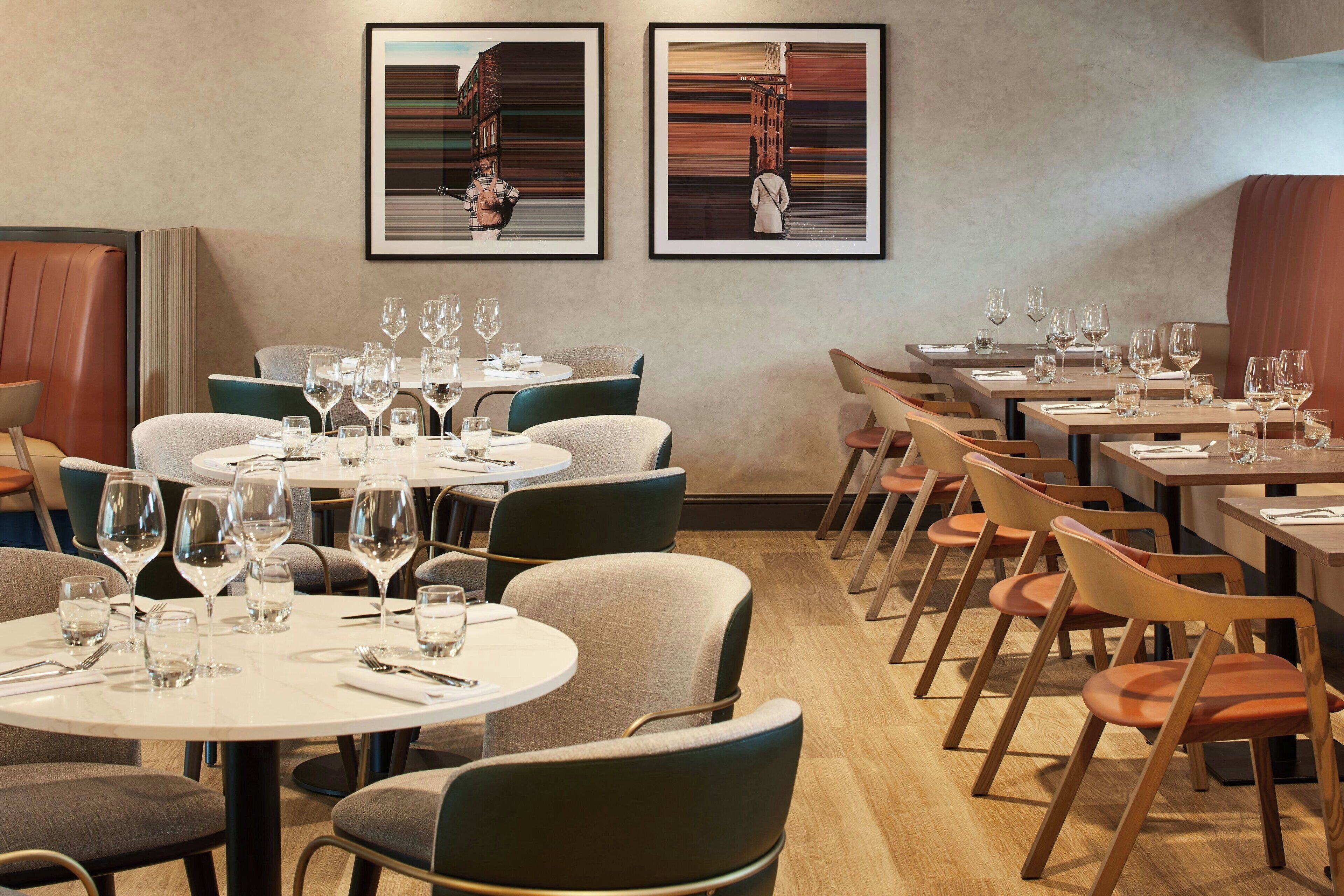 Een restaurant met ronde tafels en stoelen, kunstwerken in lijsten aan de muren, en een houten vloer.