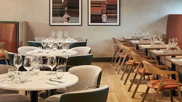 Een restaurant met ronde tafels en stoelen, kunstwerken in lijsten aan de muren, en een houten vloer.
