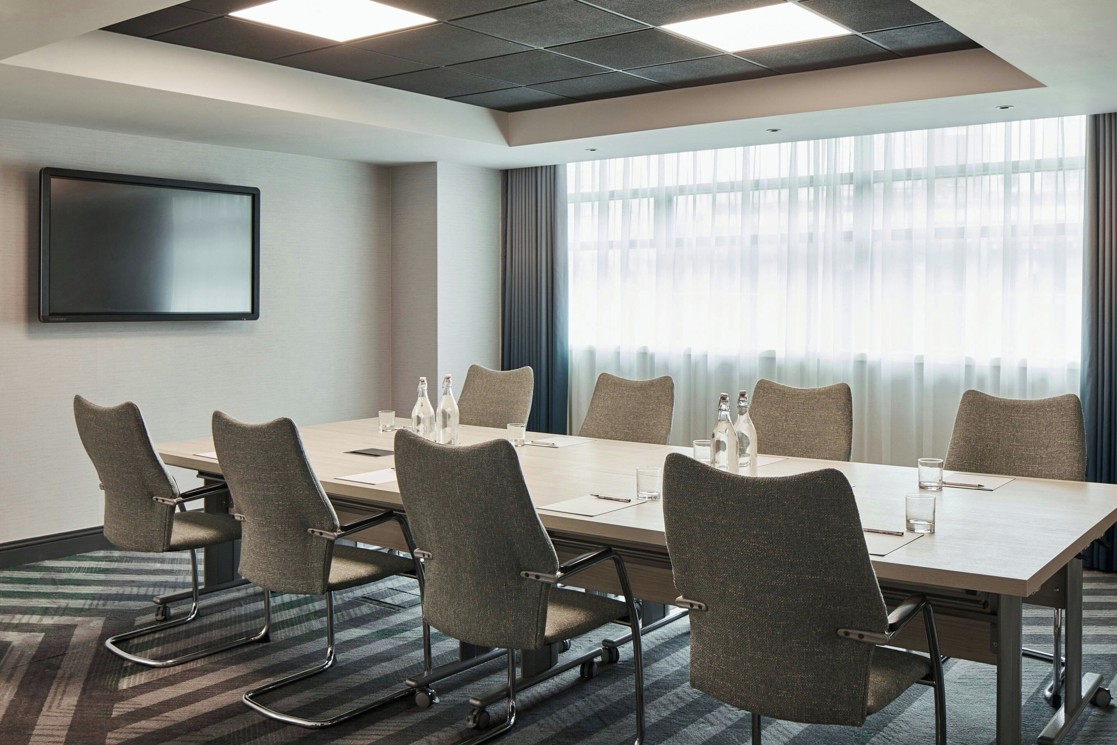 A conference room with a long table, six chairs, and a flat-screen TV on the wall.
