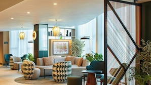A modern lobby with a sofa, chairs, and a coffee table. There are plants, a framed artwork, and a staircase with a striped railing. - Manchester Marriott Hotel Piccadilly (Manchester)