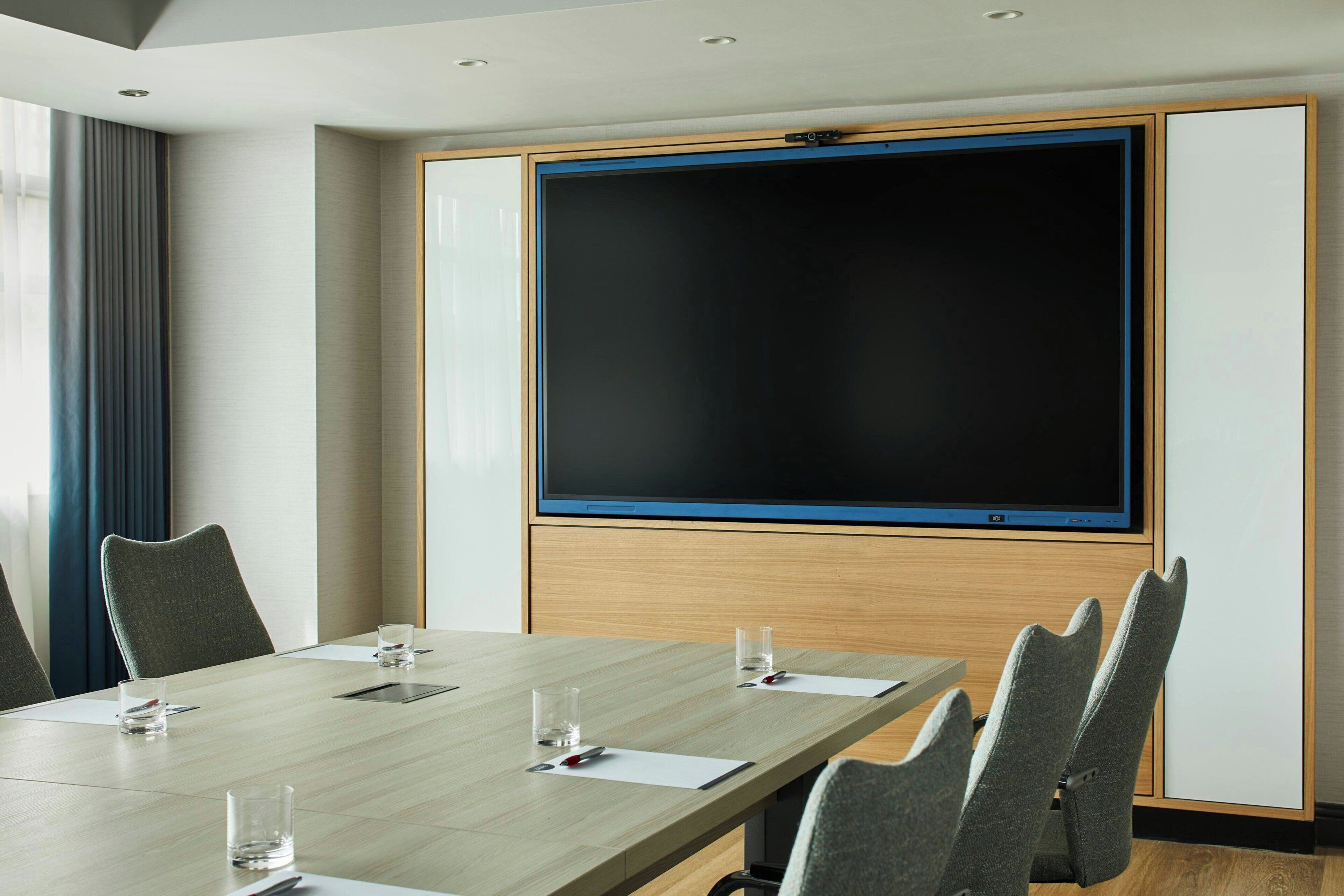 A conference room with a large screen, a long table, and several chairs.