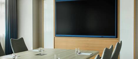 A conference room with a large screen, a long table, and several chairs.