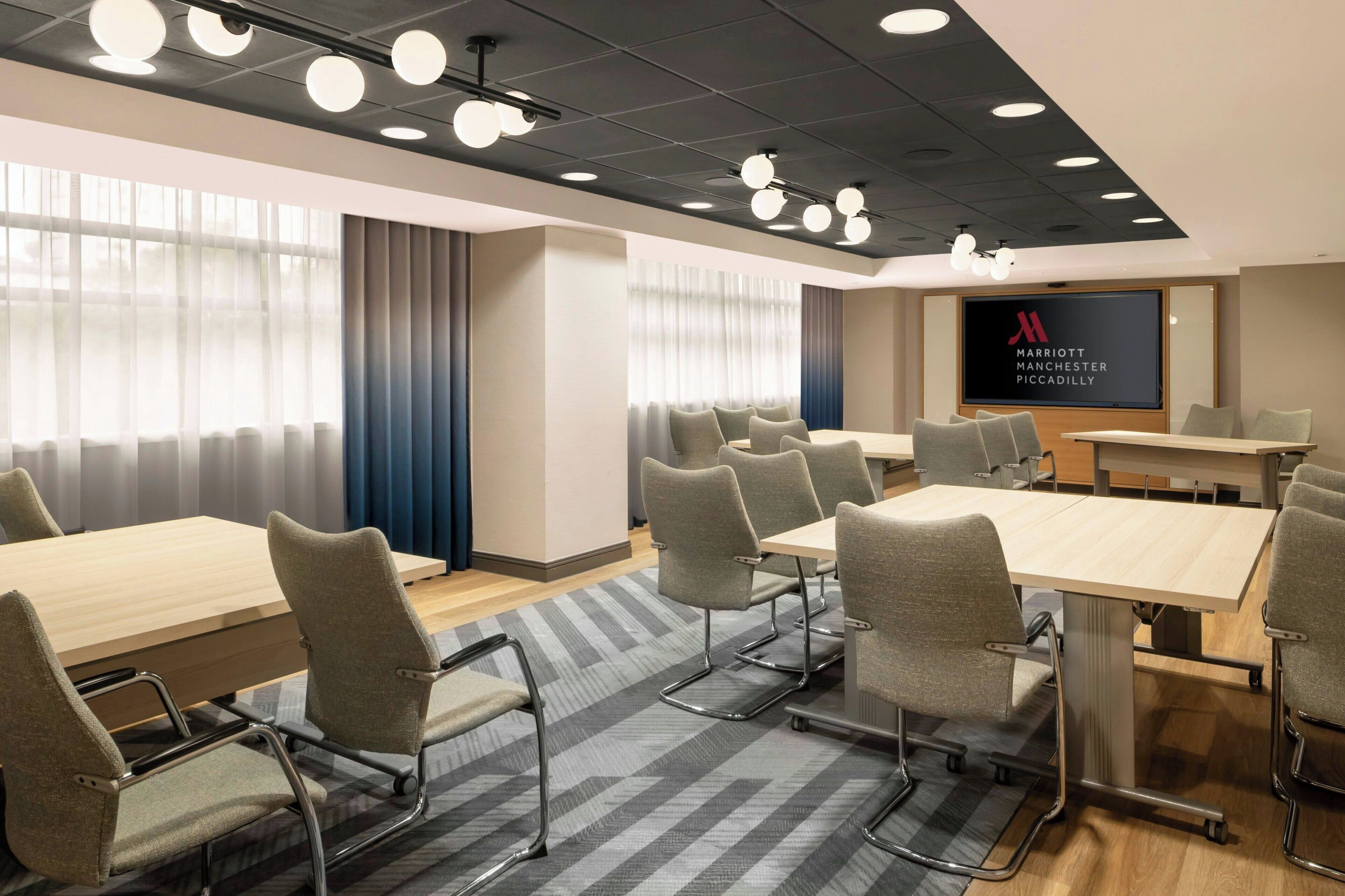 A conference room with a large screen displaying the Marriott logo, grey upholstered chairs, wooden tables, and a patterned carpet.