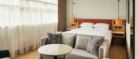 Habitación de hotel con una cama, un sofá, una mesa redonda y una silla. Hay dos mesitas de noche con lámparas.
