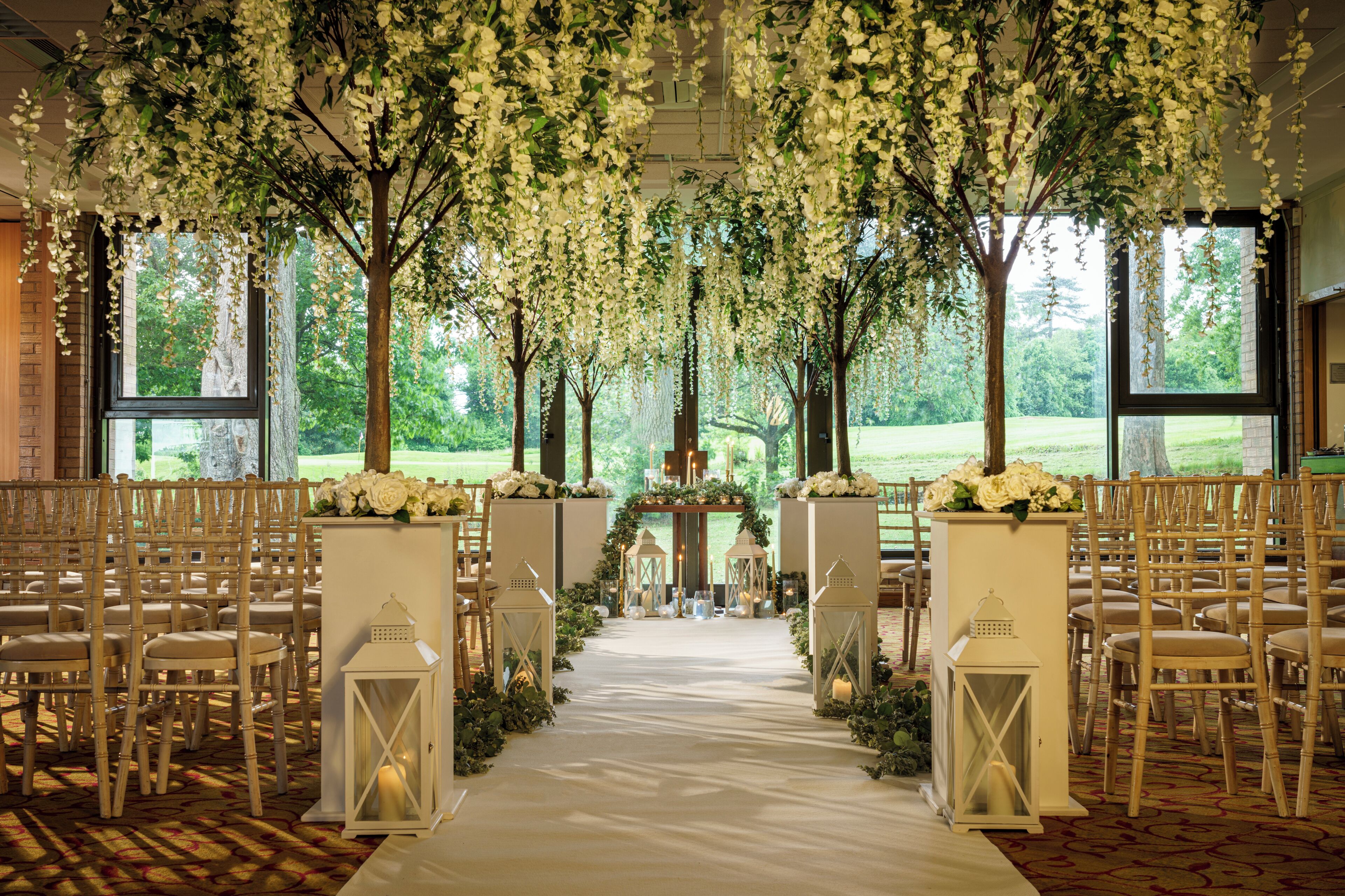 Un espacio interior con un dosel floral, hileras de sillas y un pasillo central que conduce a un escenario.