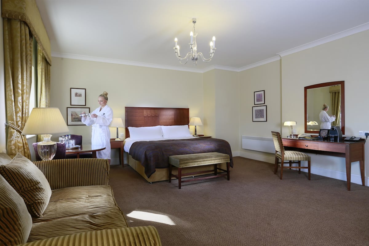 A hotel room with a bed, a desk, a chair, a sofa, a lamp, and a chandelier.