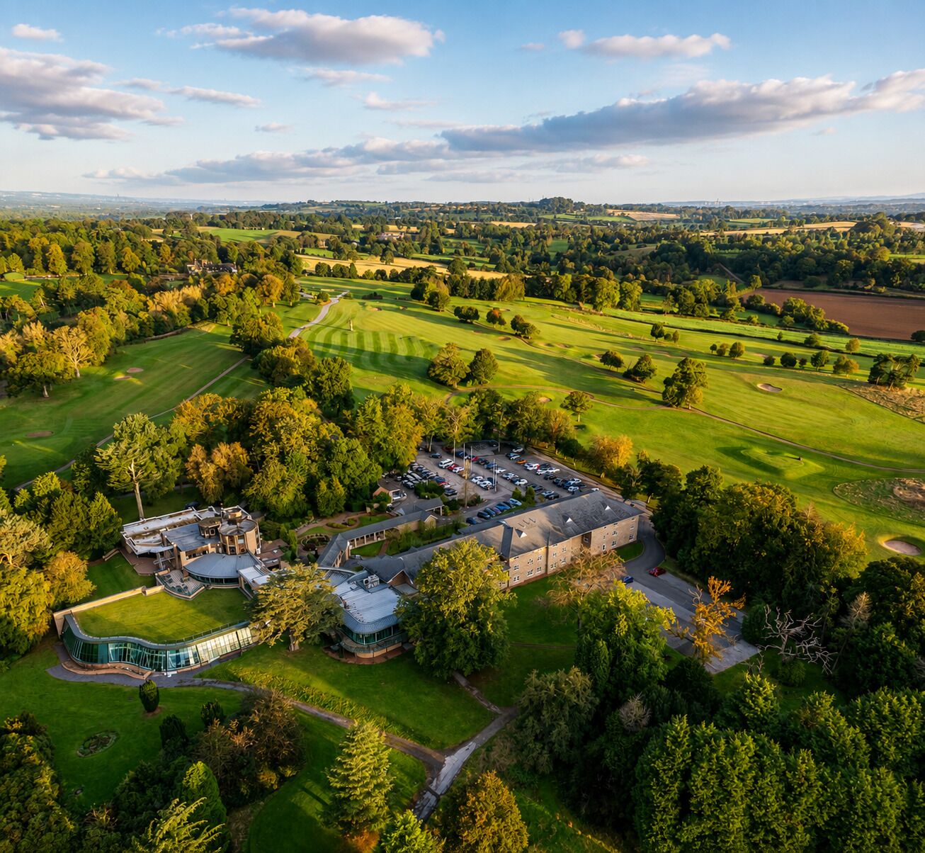 An aerial view of a golf course with a large building complex, surrounded by lush greenery and trees.