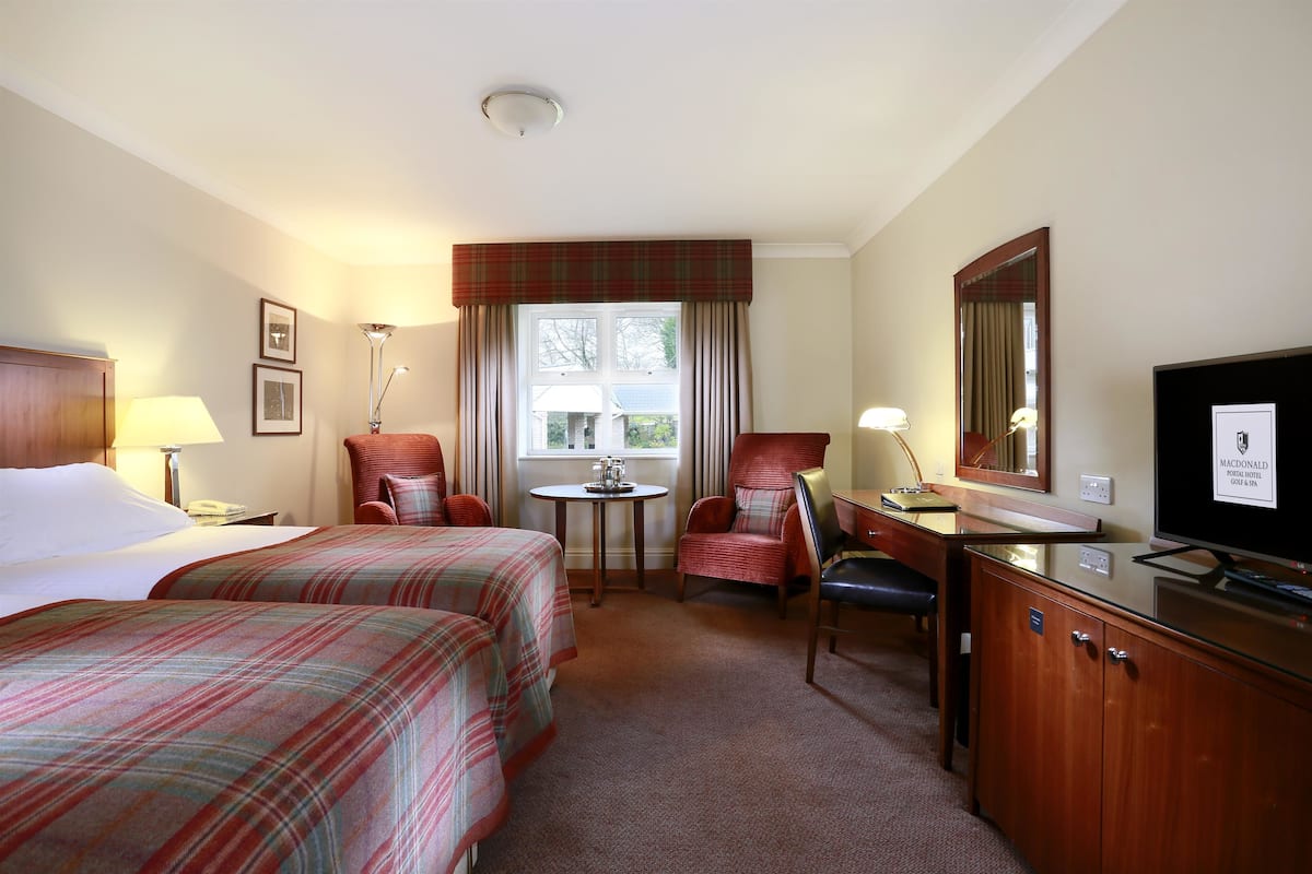 A hotel room with two beds, a desk, a chair, a television, and a window with curtains.