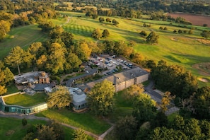 An aerial view of a golf course with a building complex, including a parking area and a clubhouse. - Macdonald Portal Hotel, Golf and Spa (Tarporley)