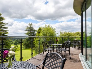 Un balcon doté de mobilier d’extérieur, d’une rambarde en verre et offrant une vue sur un paysage verdoyant.