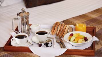 A breakfast tray with coffee, jam, bread, fruit, and juice on a bed.