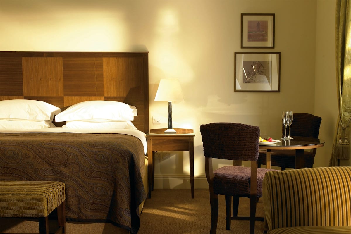 A hotel room with a bed, a chair, a table with a lamp, and a framed picture on the wall.