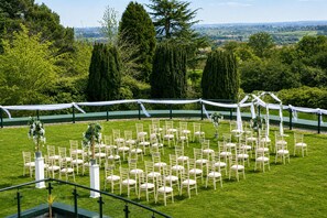 Un lieu de réception en plein air pour les mariages, avec des rangées de chaises blanches, une arche blanche et une pelouse verdoyante.