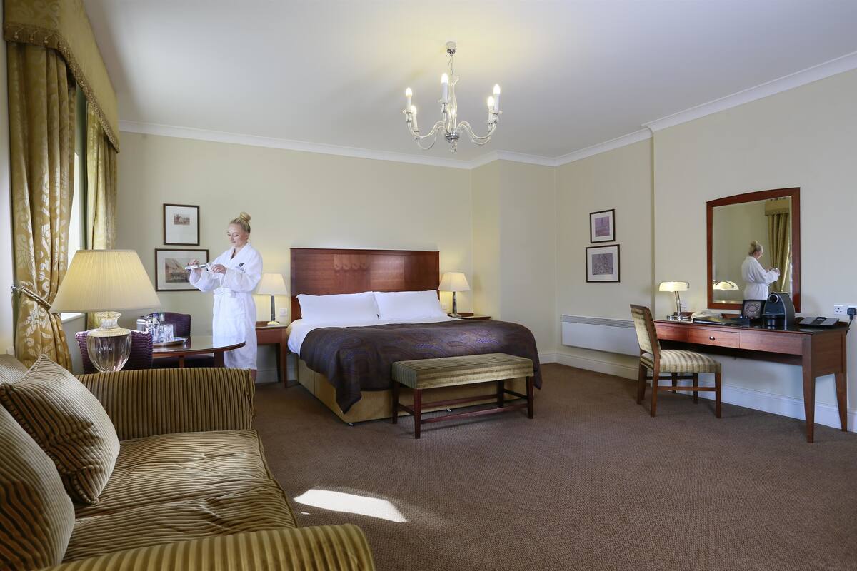 A hotel room with a large bed, a desk, a chair, a sofa, and a chandelier.