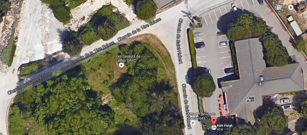 Luchtbeeld van een kustgebied met een parkeerplaats, een gebouw met de tekst 'Halt Hotel' en een groen gebied met bomen.