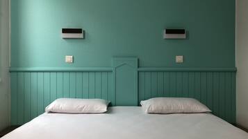 Habitación con paredes color turquesa, cabecera de madera, dos almohadas blancas y dos interruptores de luz fijos a la pared.