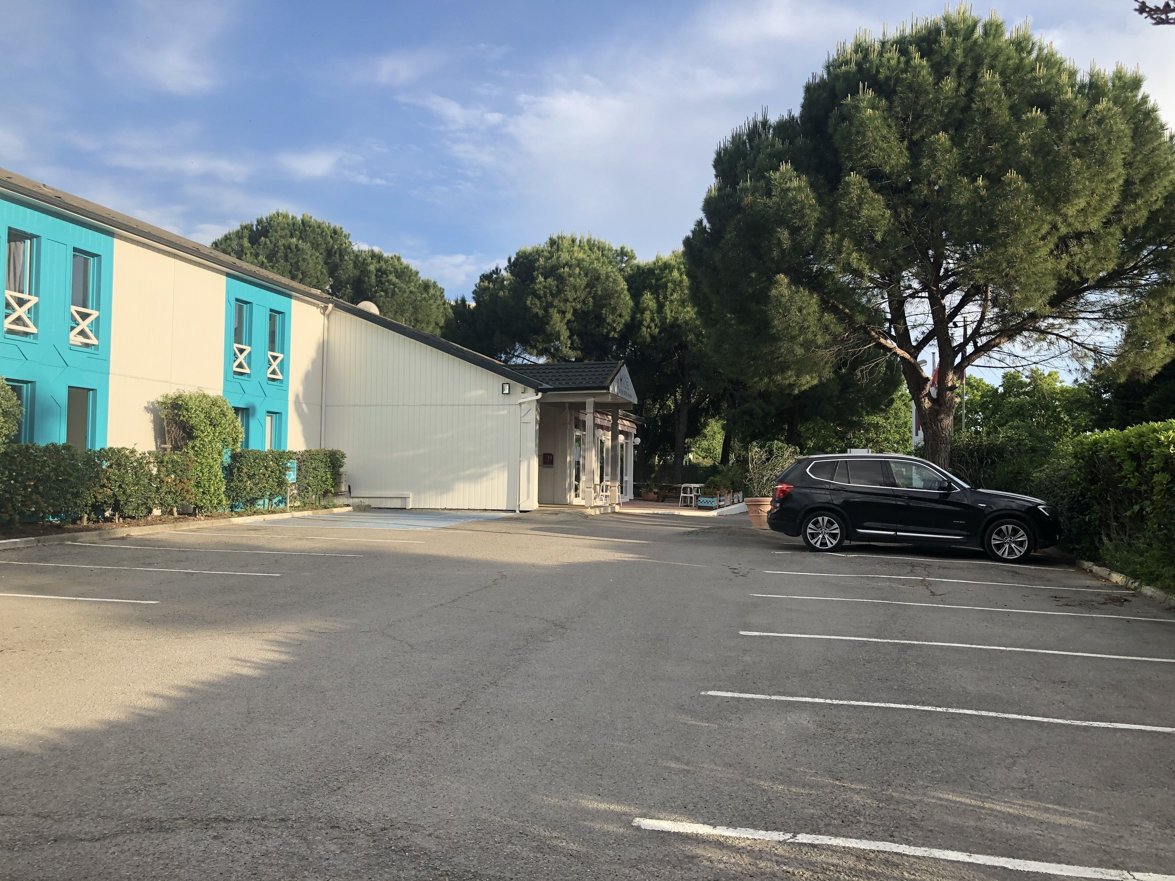 A parking lot with a building featuring blue and white exterior walls, a small entrance, and a parked black car.