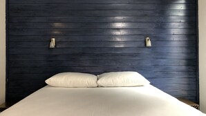 En säng med vita sängkläder och två kuddar, en mörk träfärgad sänggavel och två väggmonterade lampor.