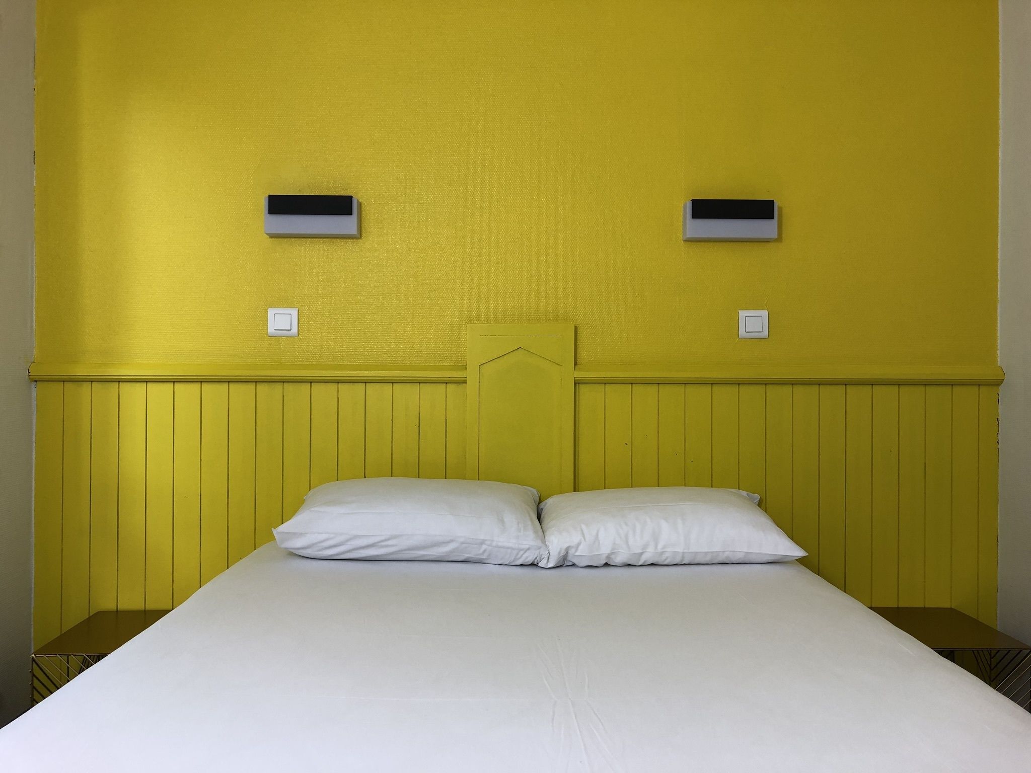 A bed with white bedding, a yellow headboard, and two wall-mounted air conditioning units.