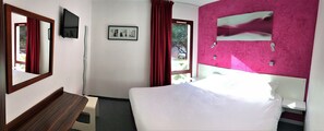 A hotel room with a bed, a desk, a chair, a window with curtains, a wall-mounted TV, and a framed picture. - Halt Hotel (Montpellier)