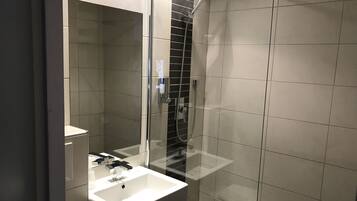 A modern bathroom with a glass-enclosed shower, a white sink, and a mirror.