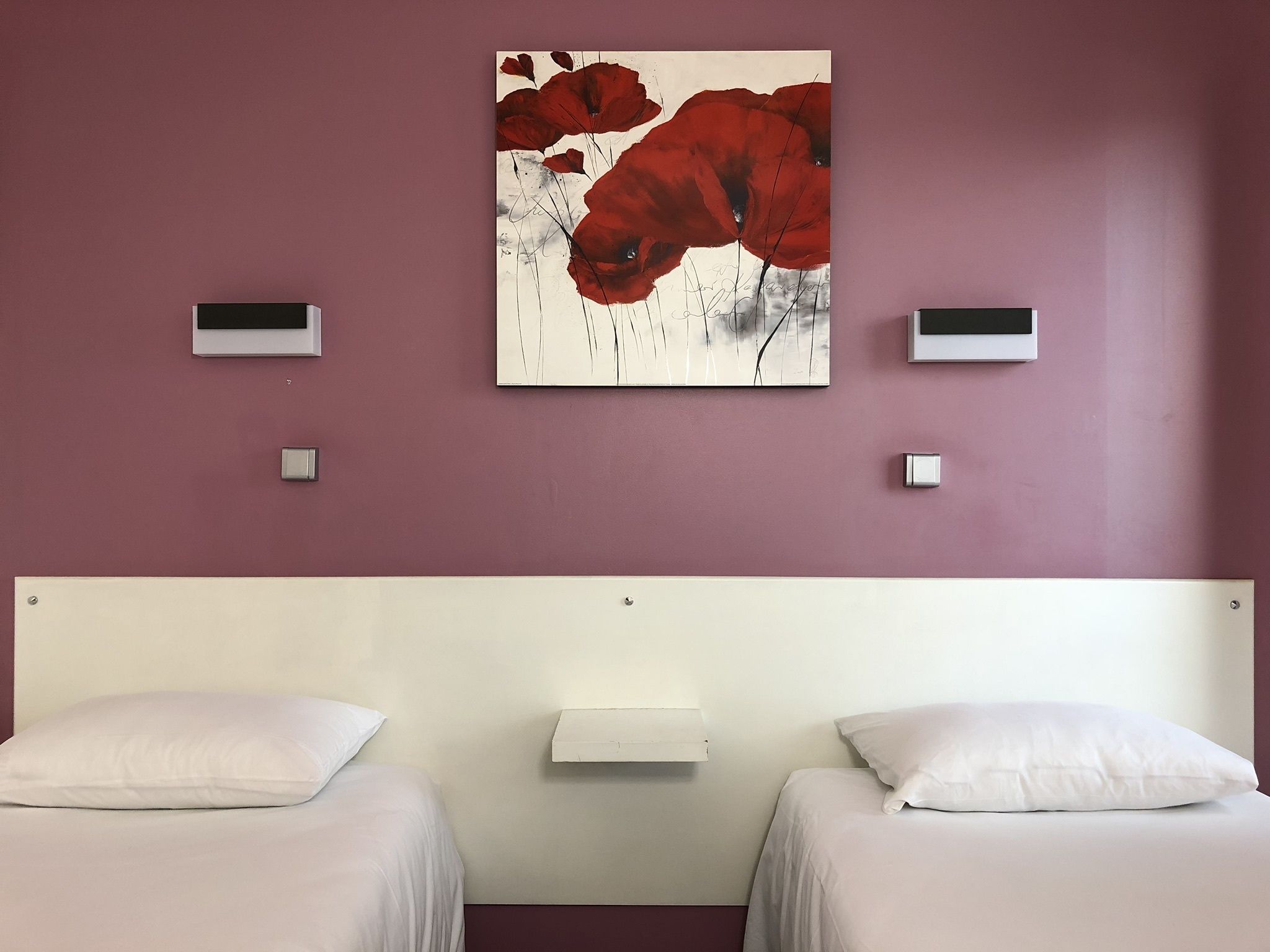 Una habitación de hotel con dos camas, un cuadro grande de flores rojas en la pared y dos mesitas de noche con interruptores de luz.