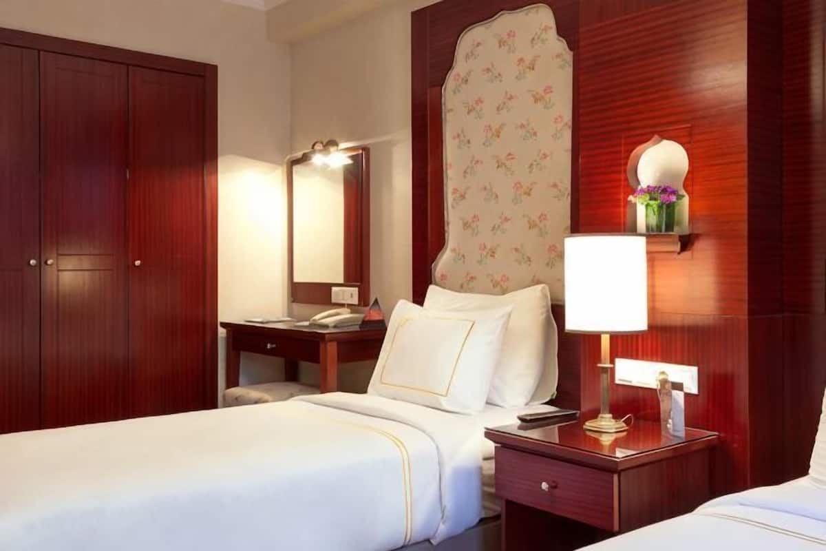 A hotel room with a bed, a desk, a chair, a wardrobe, a mirror, and a nightstand with a lamp.