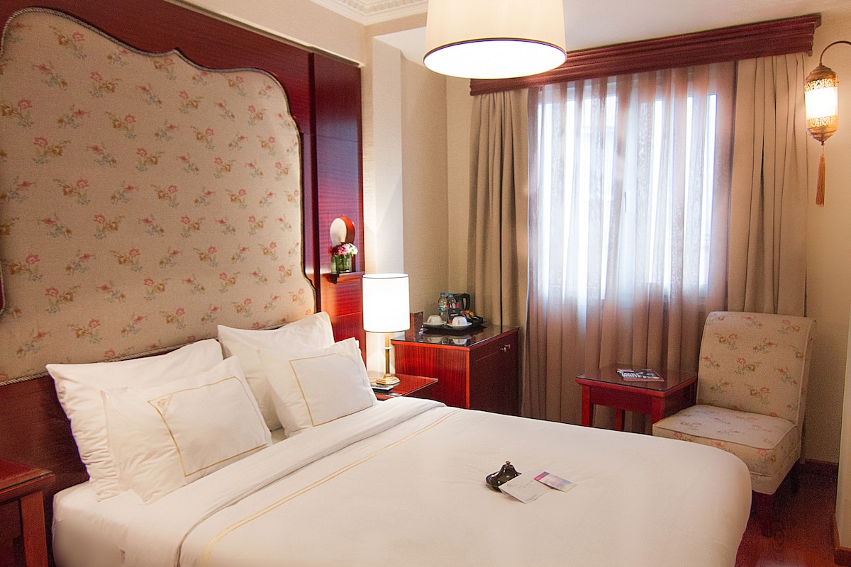 A hotel room with a large bed, a chair, a desk, and a window with curtains.
