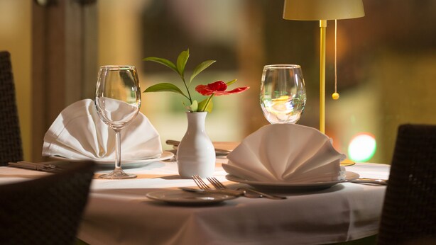 Una mesa de comedor dispuesta con un jarrón de flores rojas, una copa de vino y una lámpara.