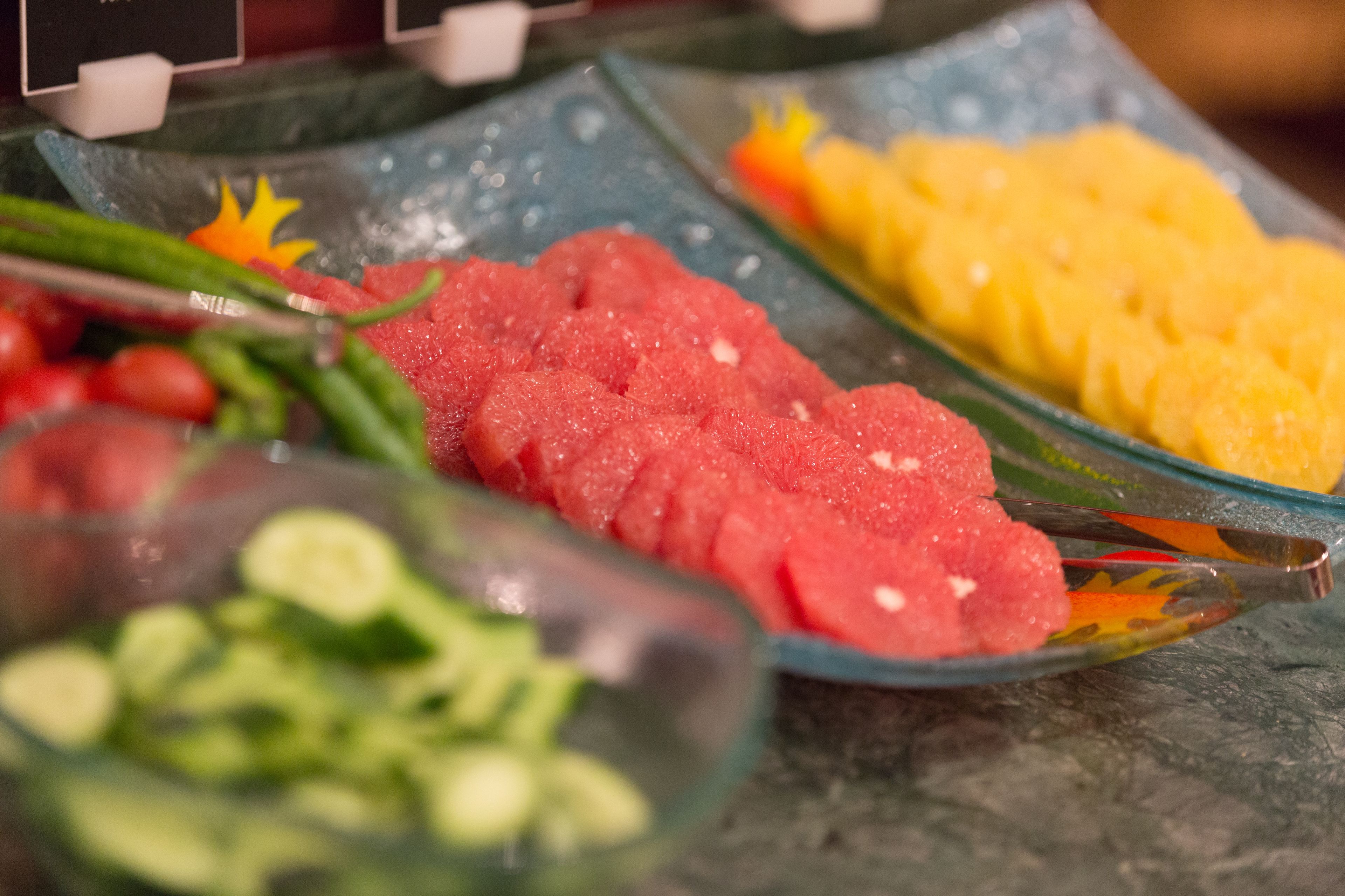 A buffet with various food items including sliced meat, yellow fruit, and green vegetables.