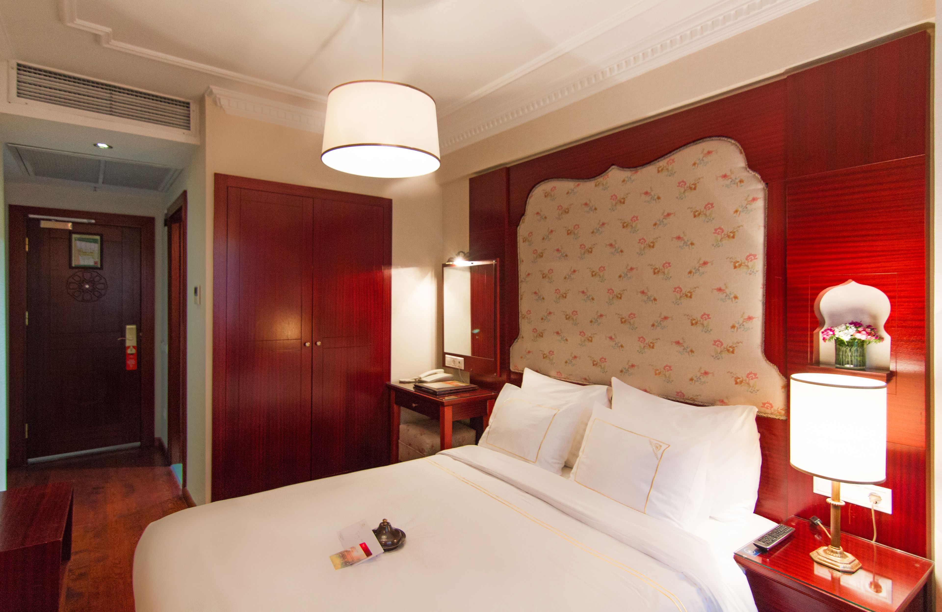 Une chambre d’hôtel avec un grand lit, une armoire en bois, un bureau avec un téléphone et une table de chevet avec une lampe.