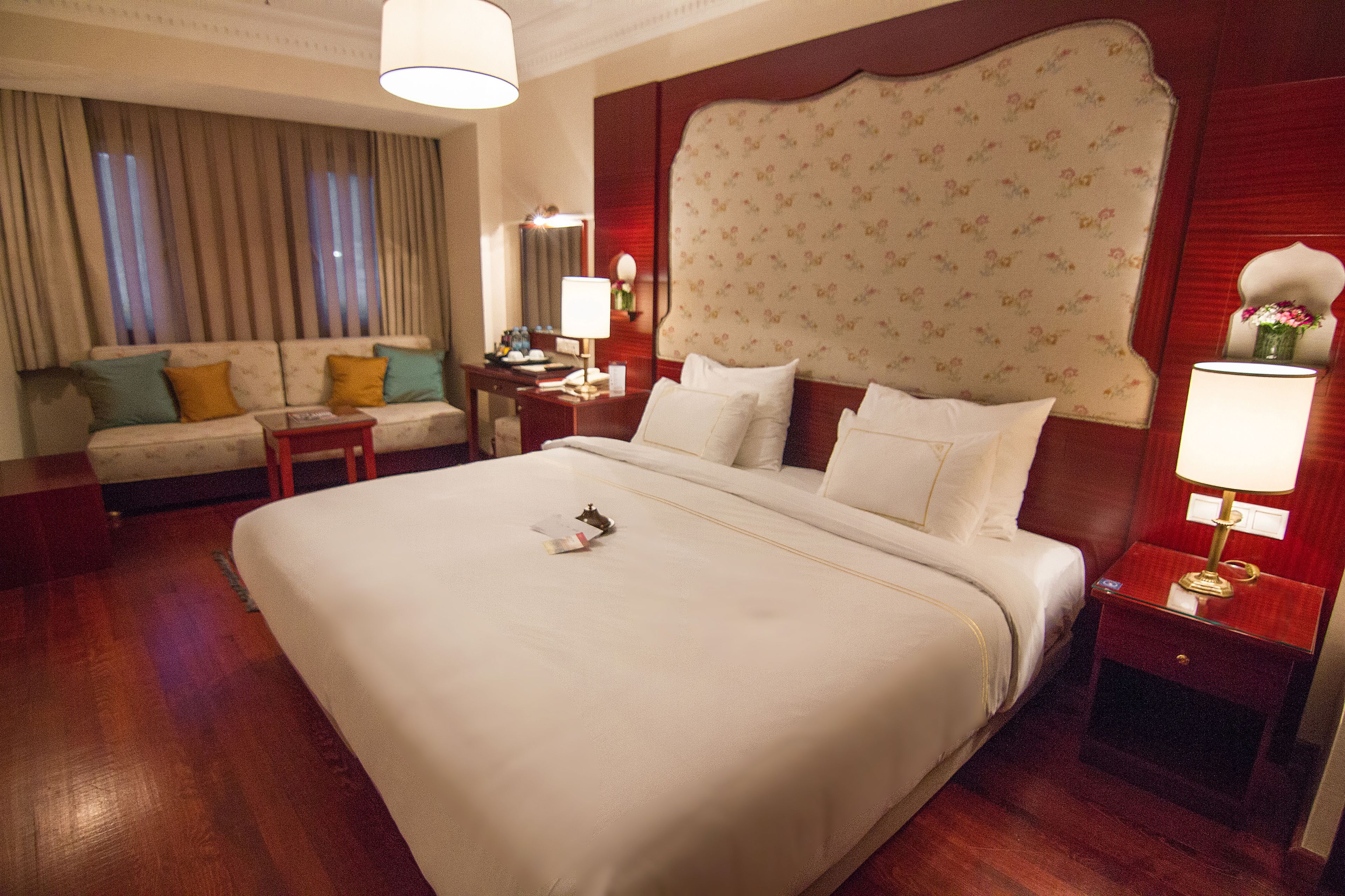 A hotel room with a large bed, a sofa, a nightstand, and a lamp.