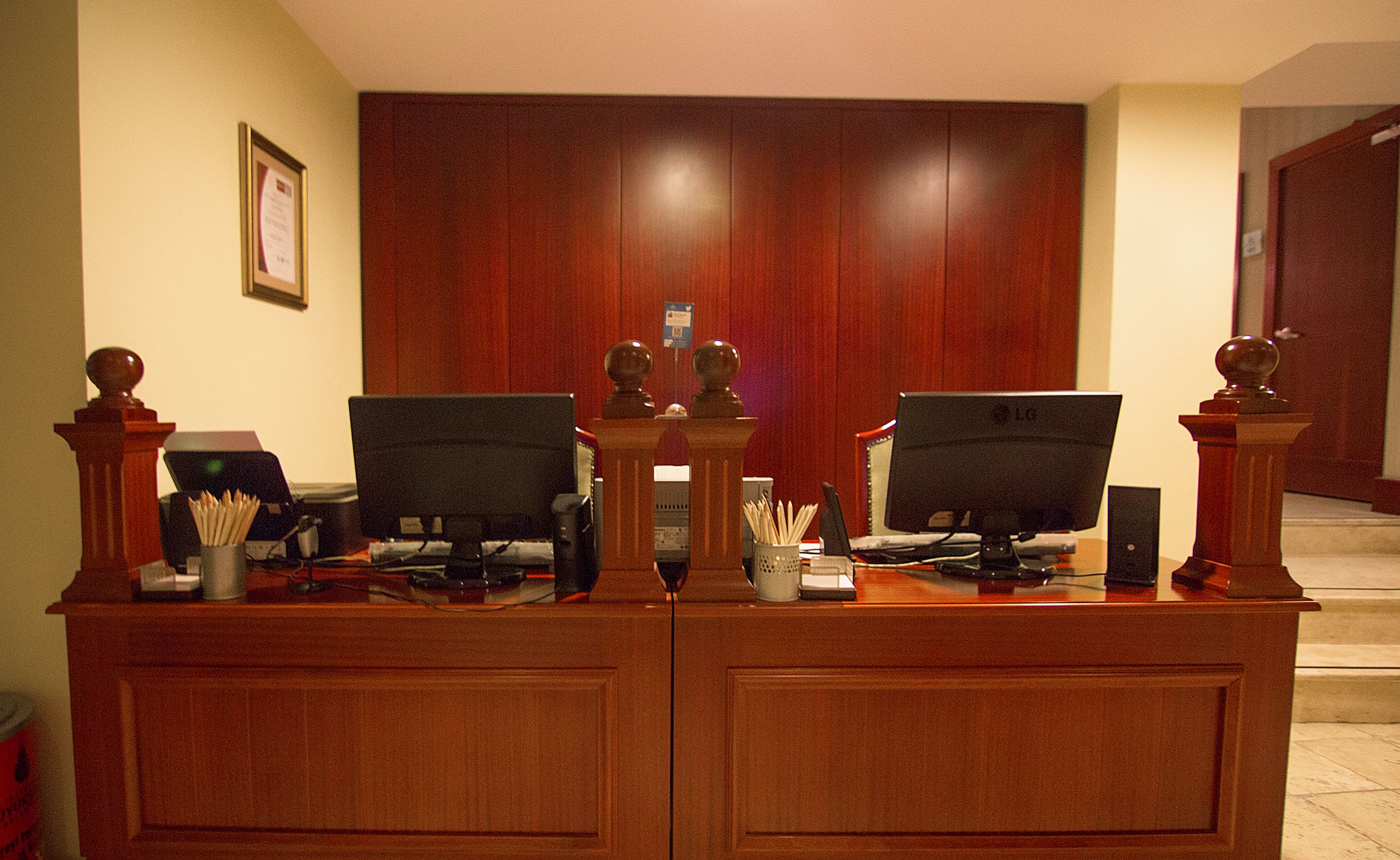 A reception desk with two monitors, a telephone, and a small desk lamp.