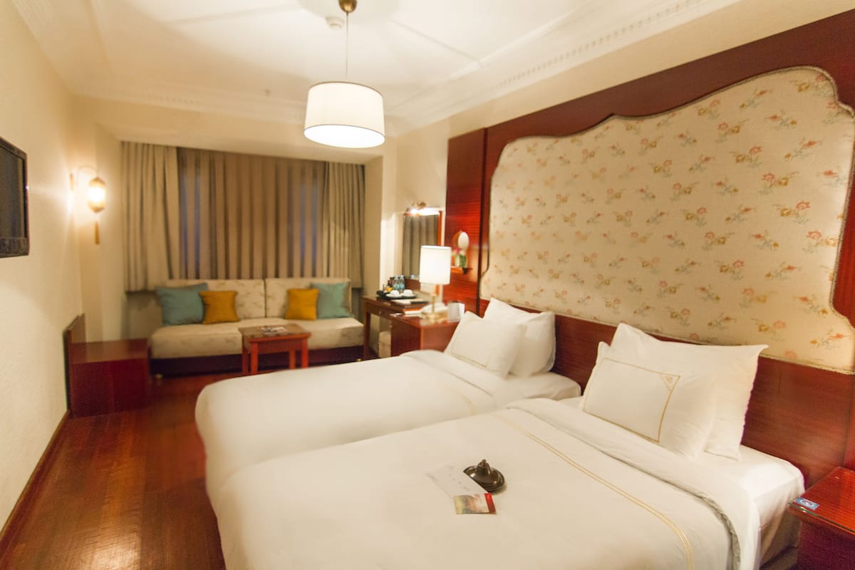 A hotel room with a large bed, a sofa, a nightstand, and a lamp.