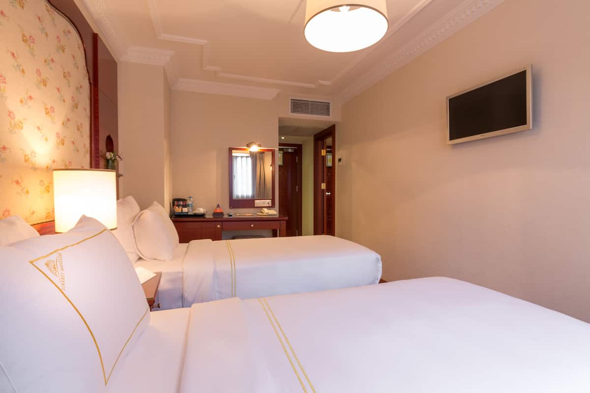 A hotel room with two beds, a desk, a TV, and a lamp.
