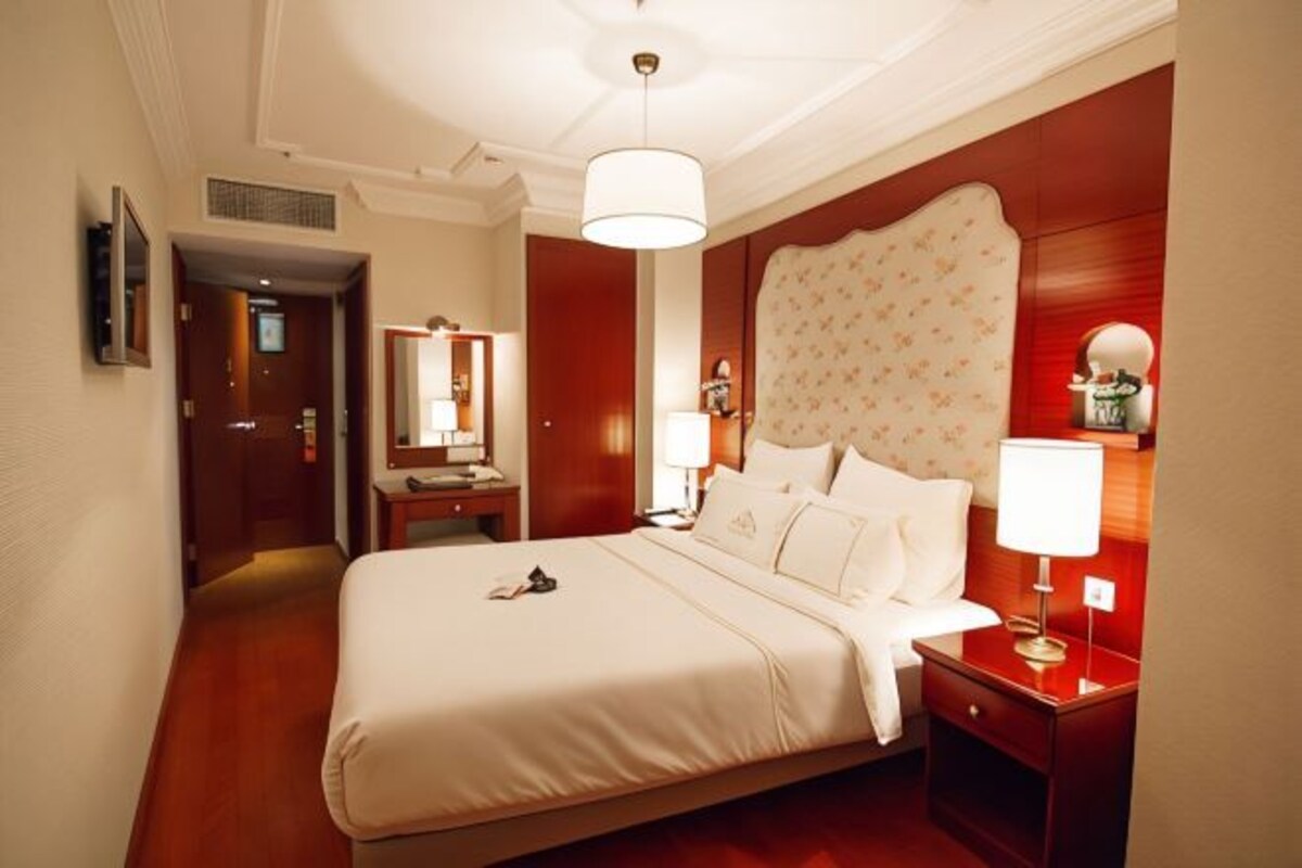 Una habitación de hotel con una cama grande, mesitas de noche, un espejo y un candelabro.