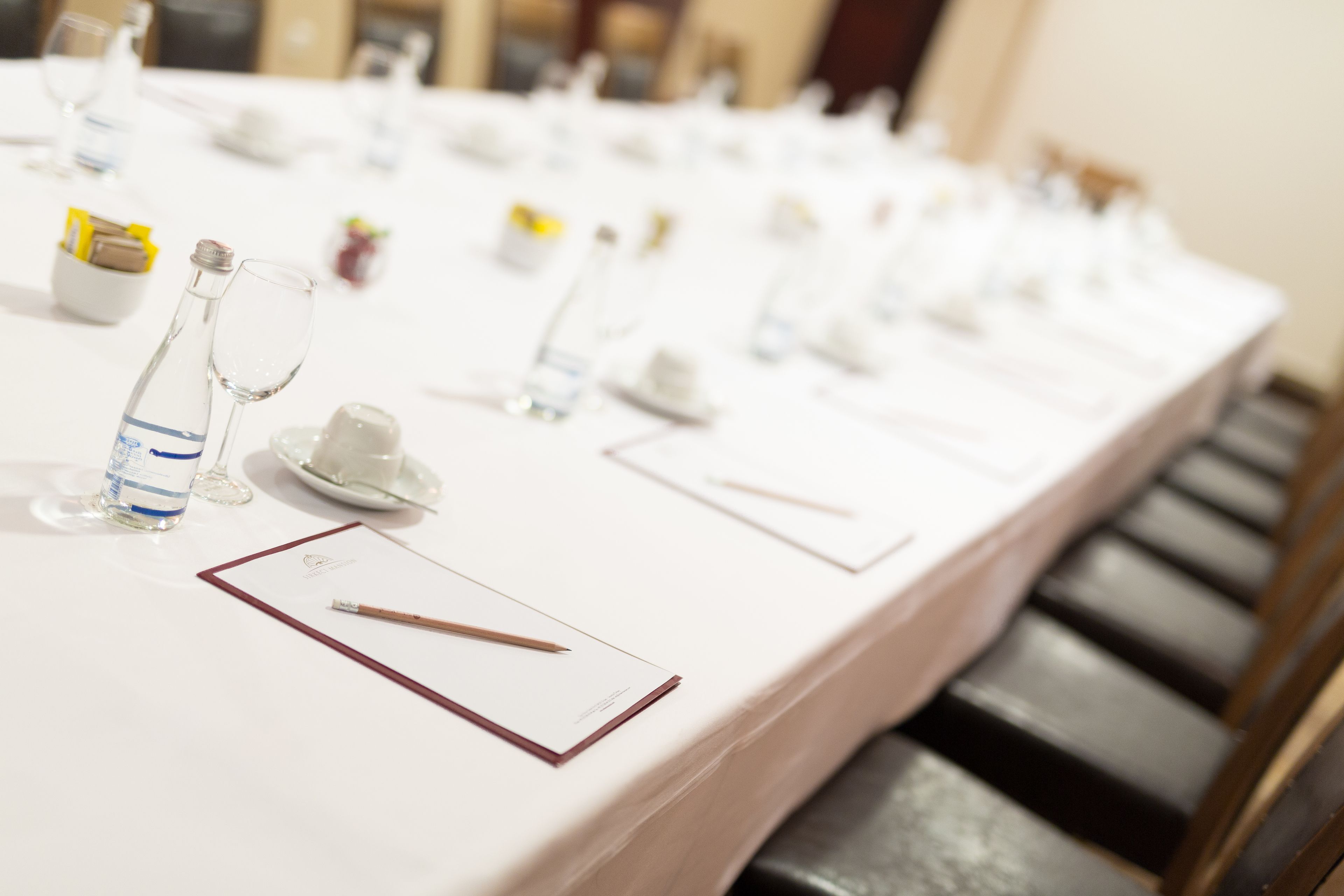 Una larga mesa dispuesta para un evento formal, con copas de vidrio transparente, platos y una botella de agua.