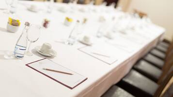 Una larga mesa dispuesta para un evento formal, con copas de vidrio transparente, platos y una botella de agua.
