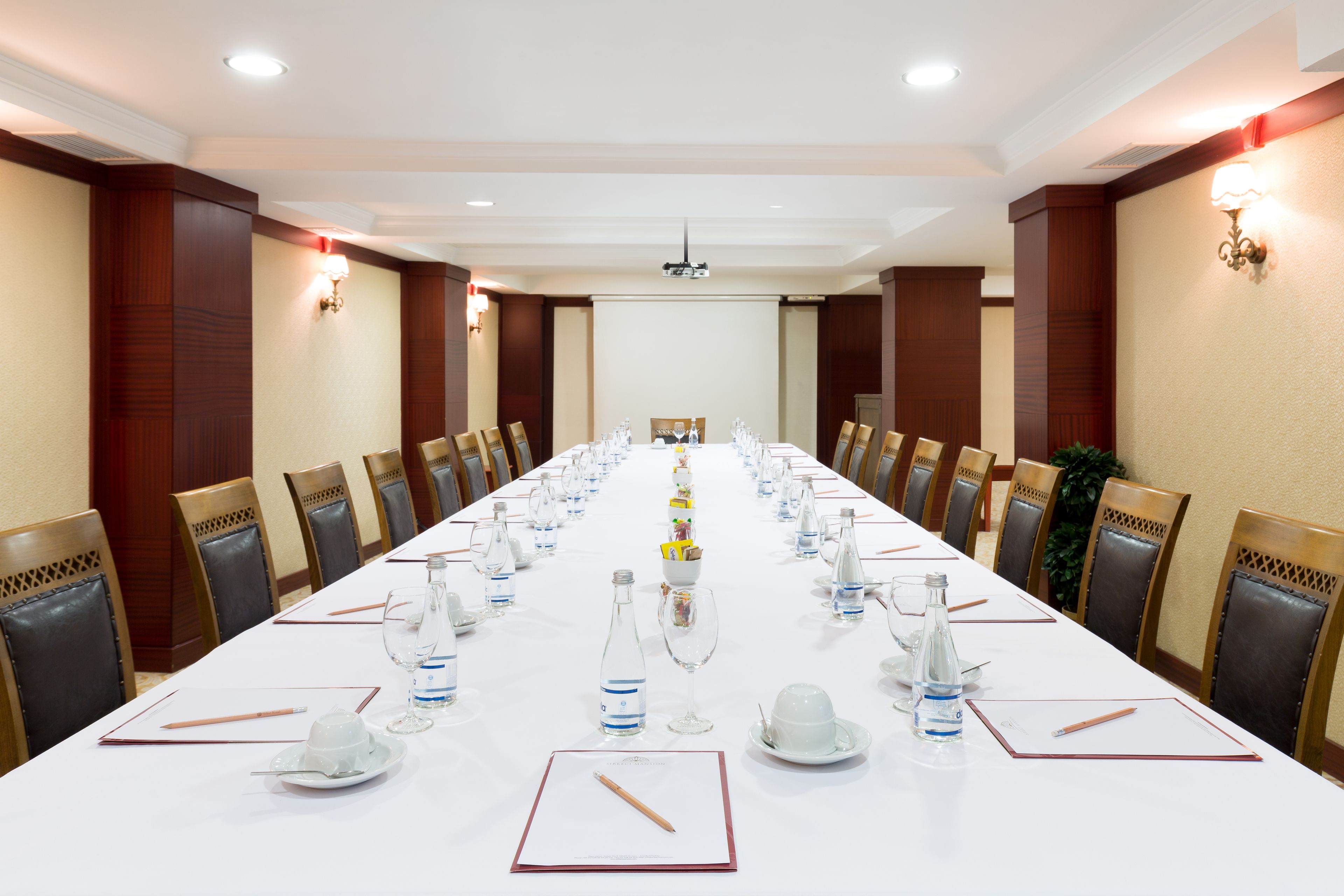 Un salón de conferencias con una larga mesa dispuesta para una reunión, equipado con sillas, botellas de agua y vasos.