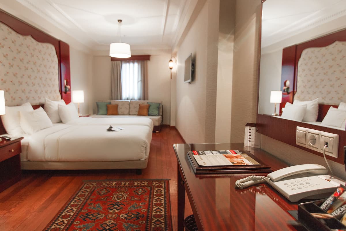 A hotel room with a large bed, a smaller sofa, a desk with a telephone, and a rug.