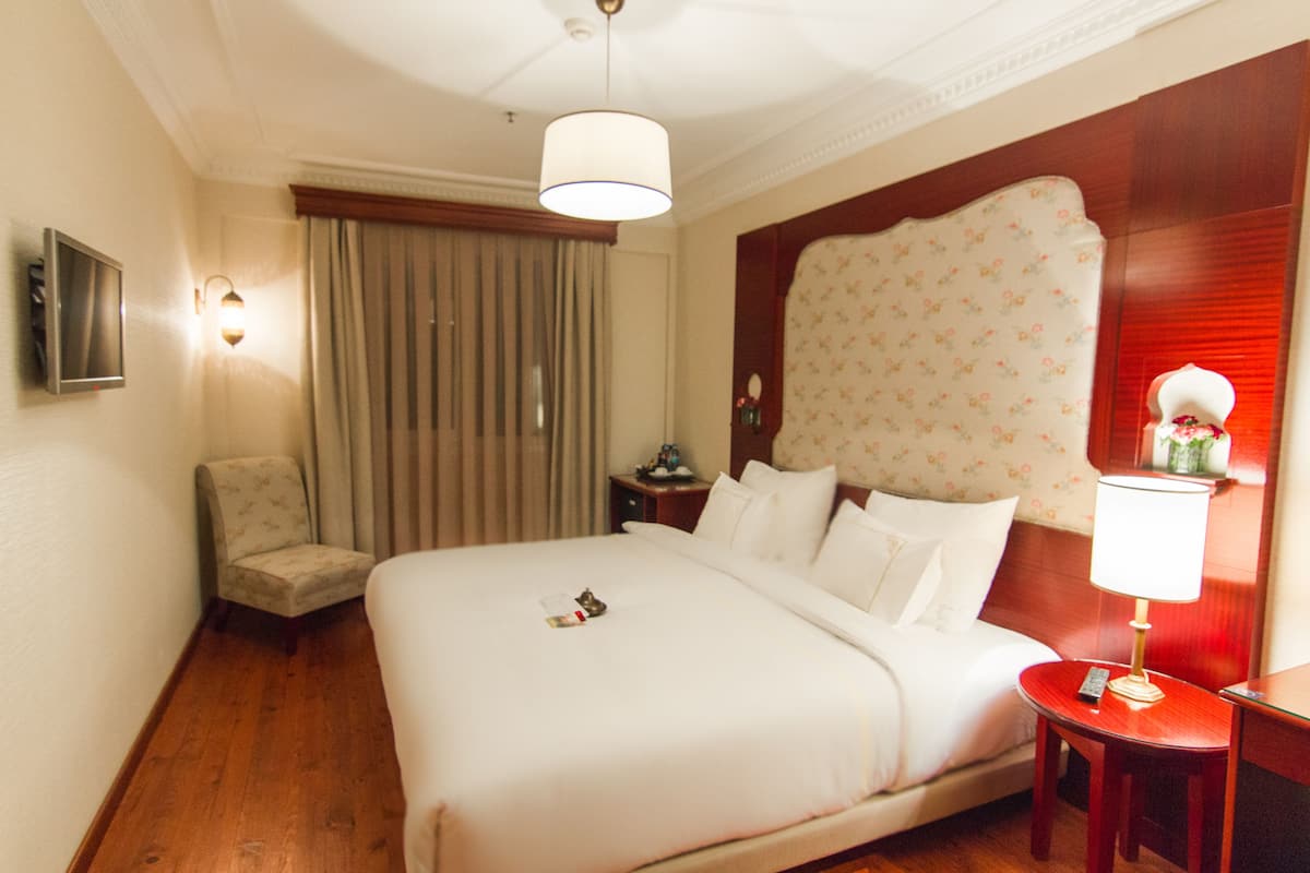A hotel room with a large bed, a chair, a nightstand, and a lamp.