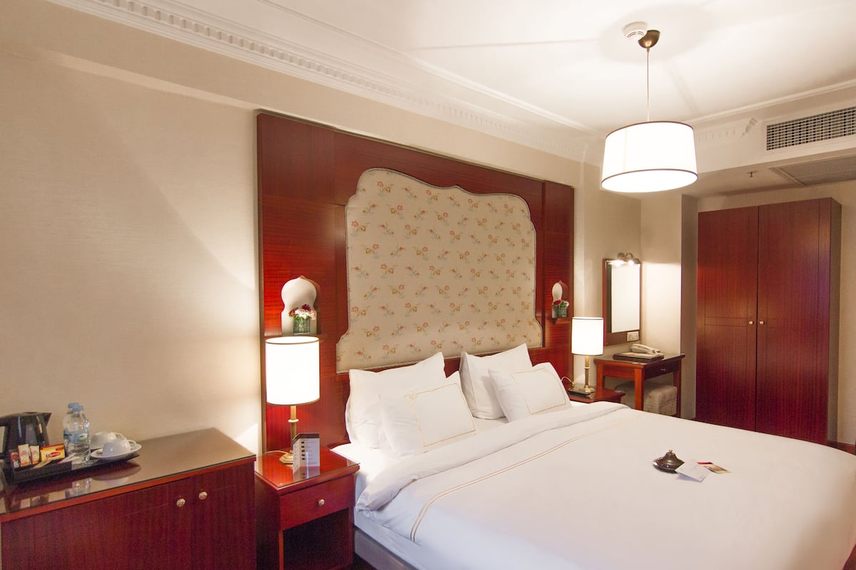 A hotel room with a large bed, two bedside tables, a nightstand, a mirror, and a wardrobe.