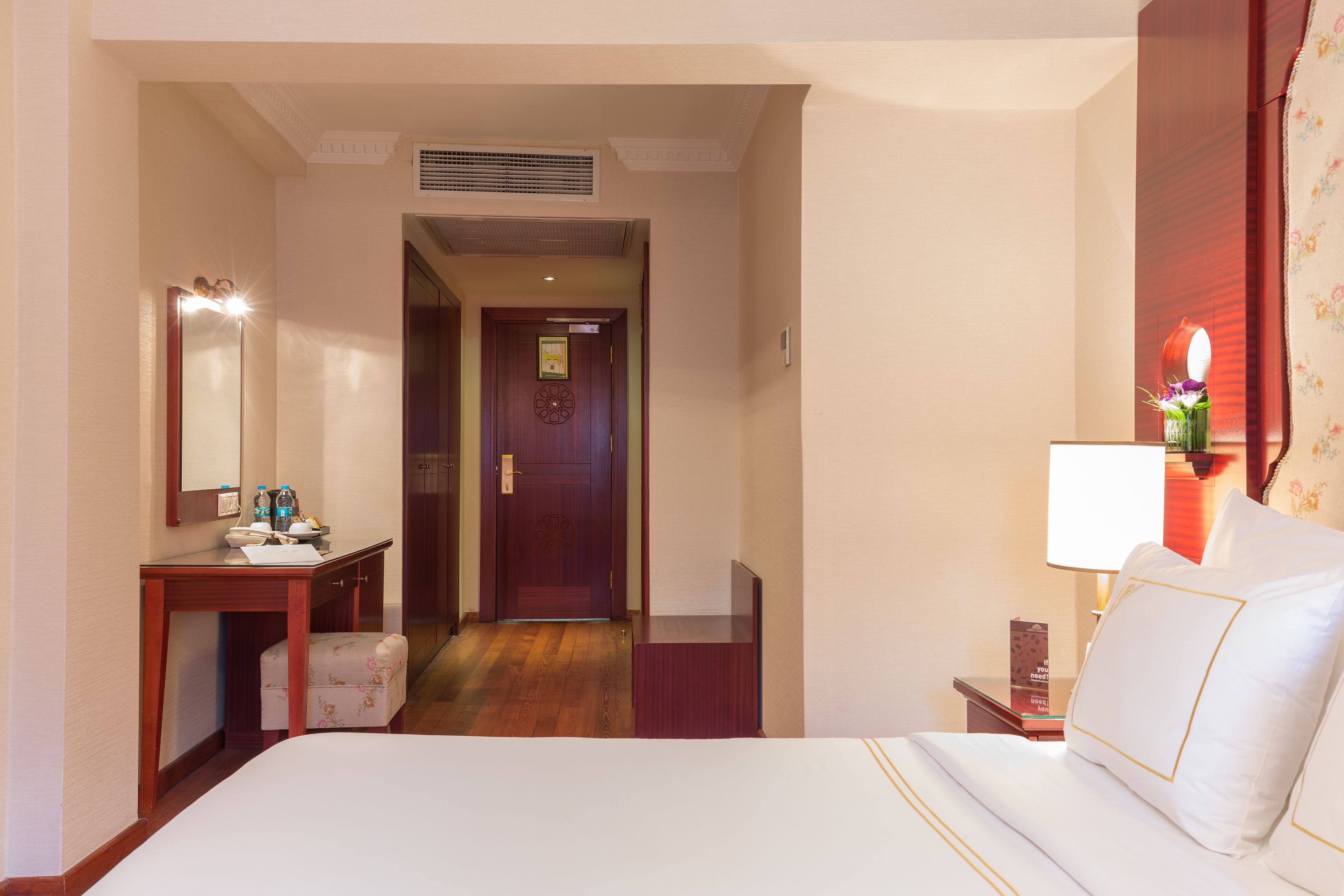 Habitación de hotel con cama, escritorio con espejo, mesita con lámpara y puerta que da a otra habitación.