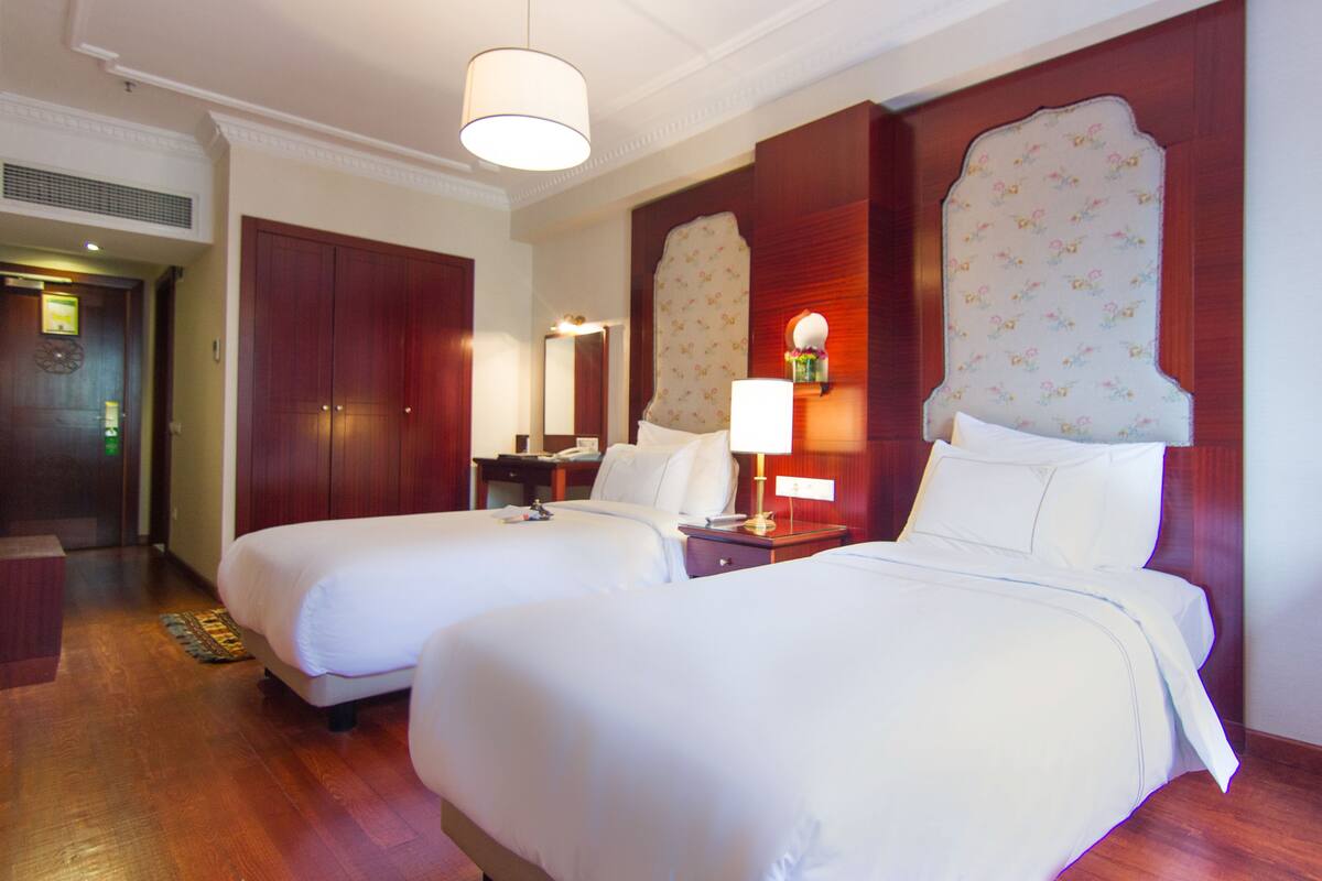 A hotel room with two beds, wooden flooring, a large mirror, and a wooden headboard with floral patterns.