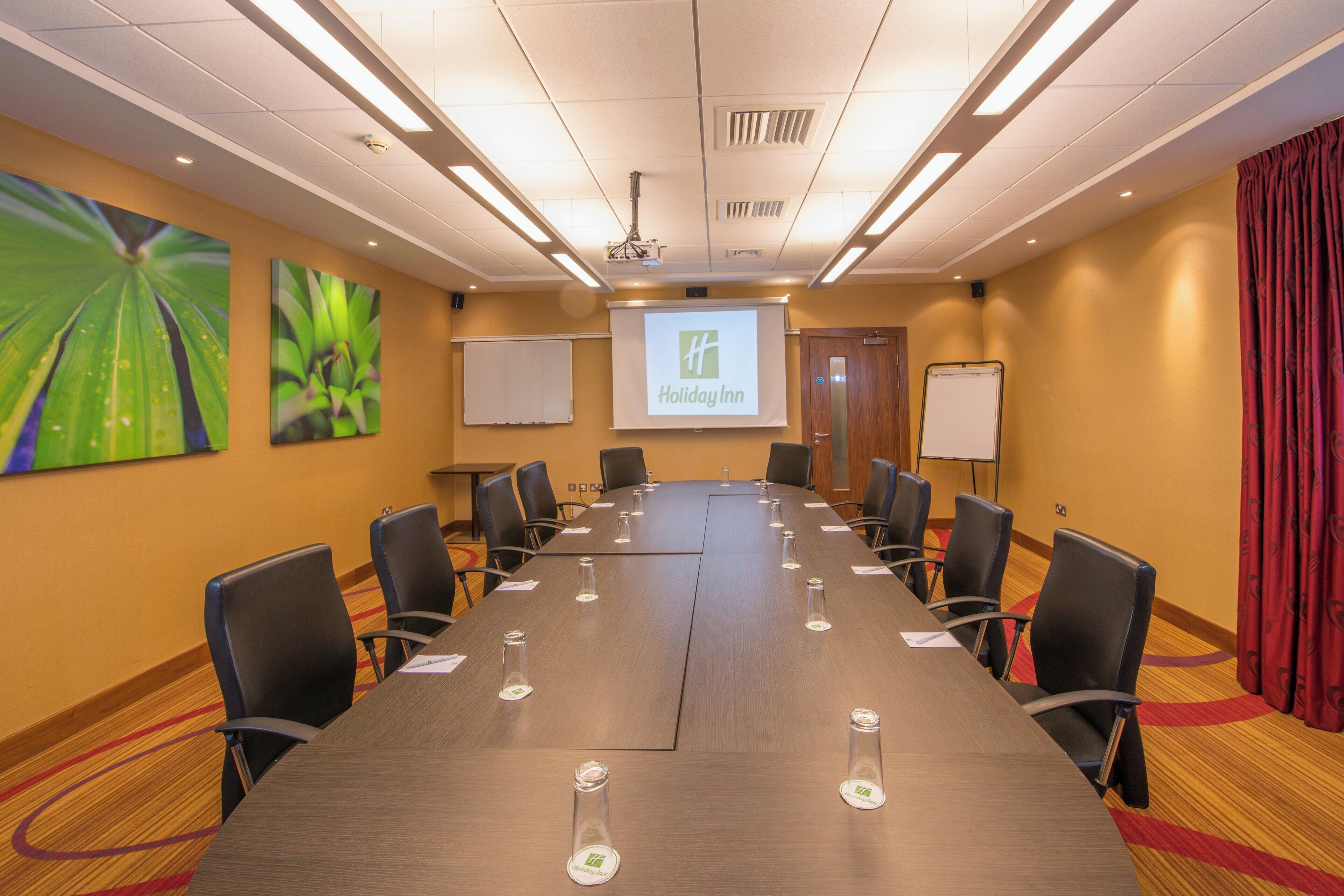A conference room with a long table, chairs, a projector screen, and a Holiday Inn banner.